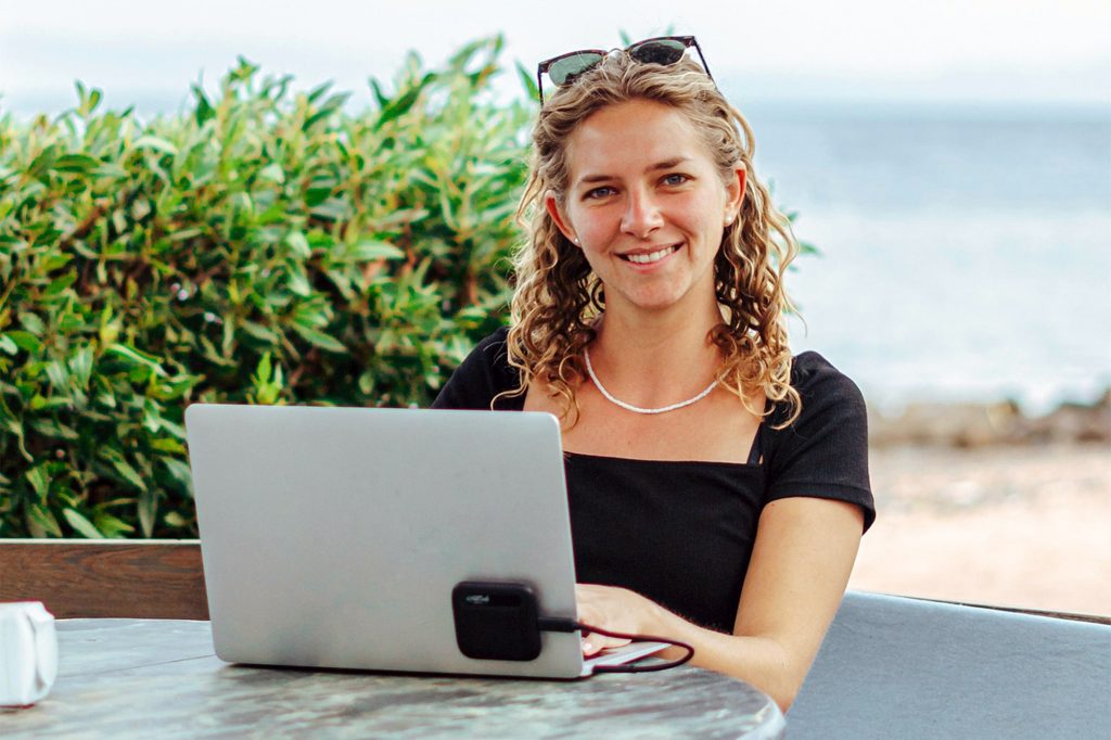 Lady smiling with her laptop and a beach in background